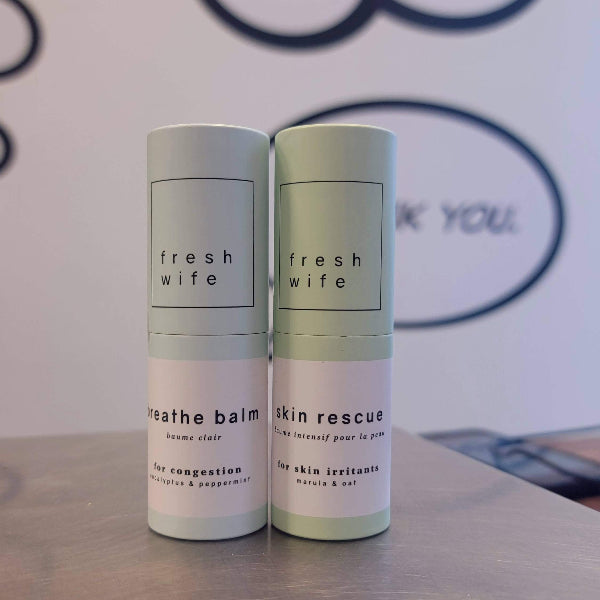 Two skincare products from 'fresh wife' on a surface with a blurred background.